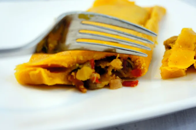 A fork cutting into an unwrapped hallaca, showing the golden corn dough and meat filling inside