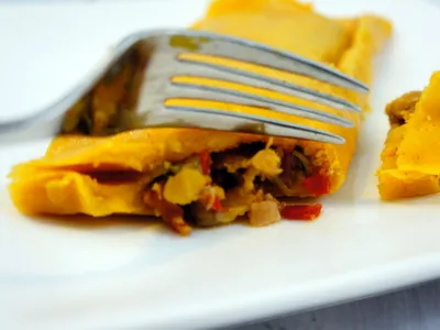 A fork cutting into an unwrapped hallaca, showing the golden corn dough and meat filling inside
