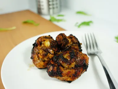 Three seared, dark-glazed chicken drumsticks on a white plate with a fork