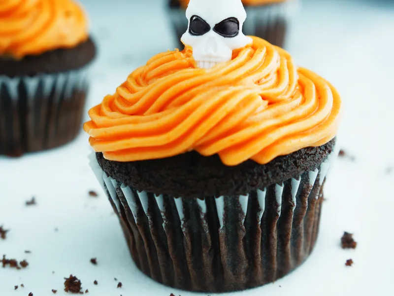 A chocolate cupcake topped with swirled orange frosting and a white sugar skull decoration