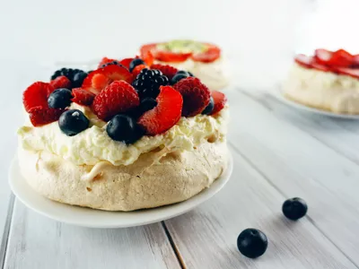 An individual pavlova topped with whipped cream, blackberries, blueberries, raspberries, and strawberries, with more pavlovas in the background