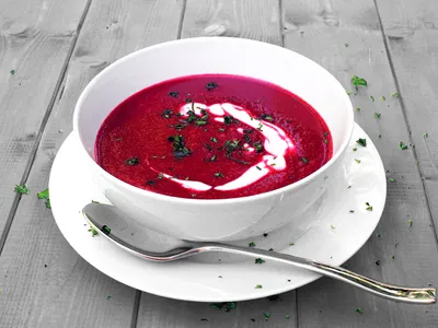 A bowl of bright pink beet soup swirled with sour cream and topped with chopped parsley