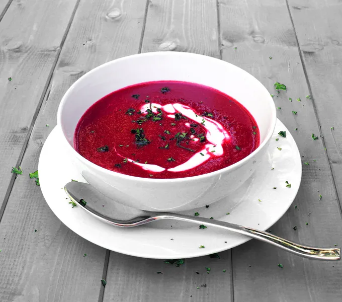 A bowl of bright pink beet soup swirled with sour cream and topped with chopped parsley