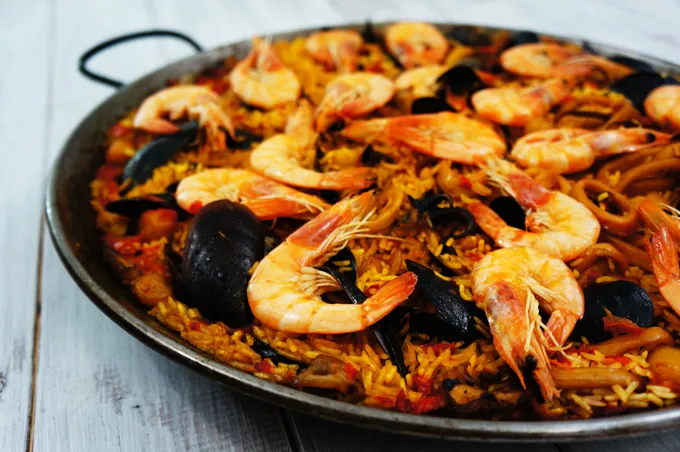Close-up of a paella pan loaded with saffron rice, shrimp, and mussels