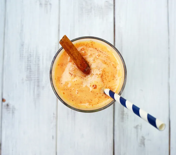An overhead view of a papaya shake in a glass topped with a cinnamon stick, with a striped straw