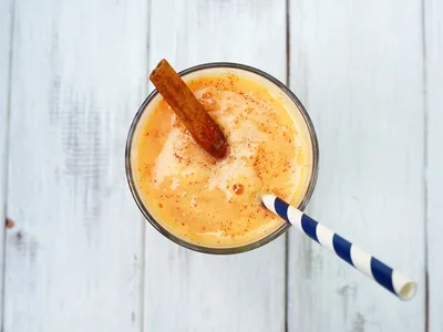 An overhead view of a papaya shake in a glass topped with a cinnamon stick, with a striped straw