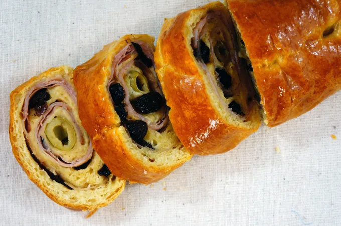 Sliced Pan de Jamon showing spiraled layers of ham, olives, and raisins inside golden bread