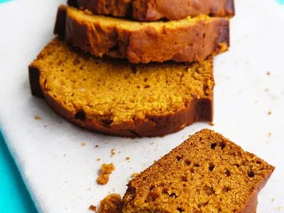 Sliced pumpkin bread on a cutting board with a bitten piece in front