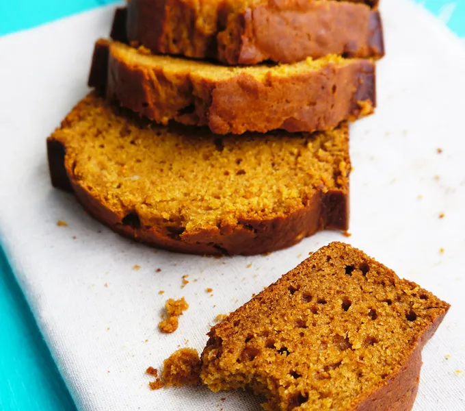 Sliced pumpkin bread on a cutting board with a bitten piece in front