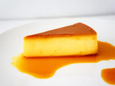 A slice of quesillo flan on a white plate pooled with amber caramel sauce