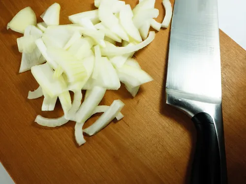 Chopped onion on a wooden cutting board next to a chef's knife