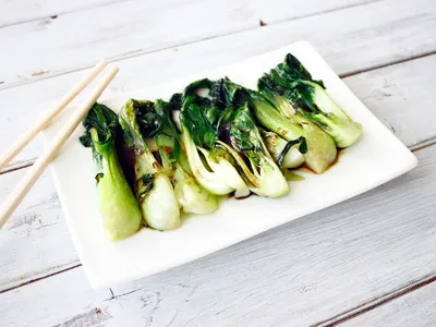 Sauteed baby bok choy drizzled with soy sauce, served on a white rectangular plate with chopsticks