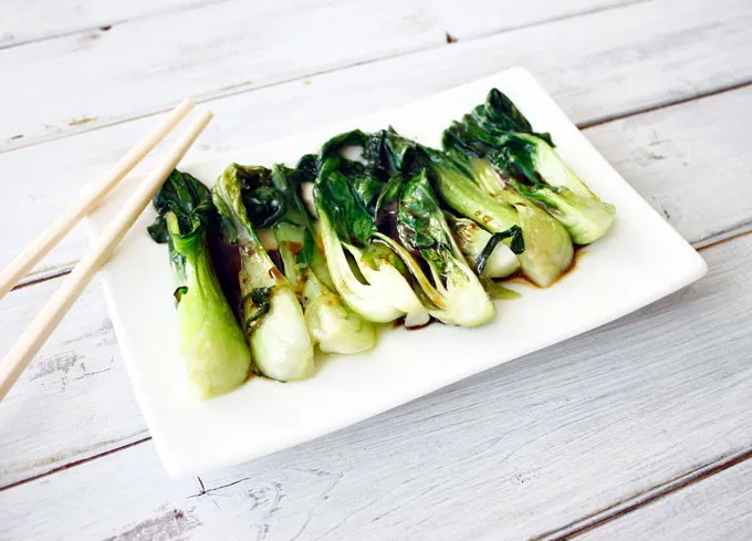 Sauteed baby bok choy drizzled with soy sauce, served on a white rectangular plate with chopsticks