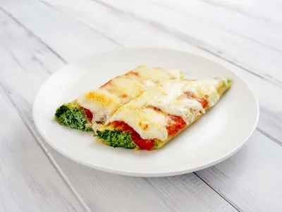 Two stuffed cannelloni topped with tomato sauce, bechamel, and melted parmesan on a white plate