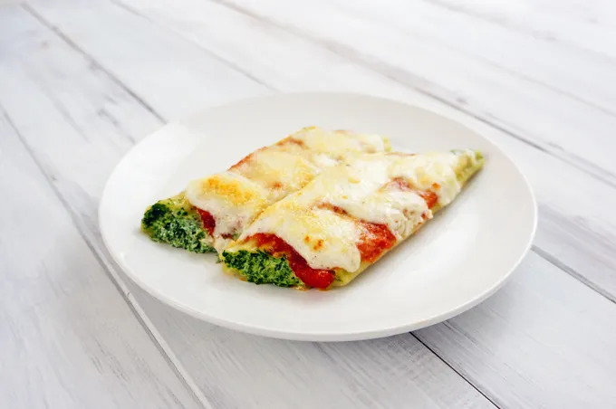 Two stuffed cannelloni topped with tomato sauce, bechamel, and melted parmesan on a white plate