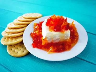 A block of cream cheese topped with red and orange pepper jelly on a plate, with crackers on the side