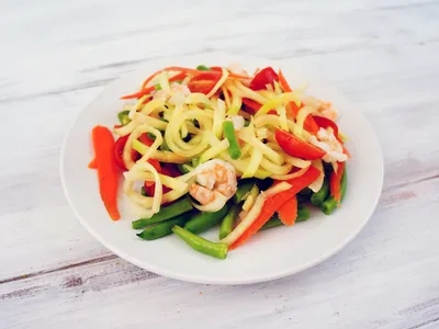 A plate of green papaya salad with shredded papaya, carrots, green beans, tomatoes, and shrimp