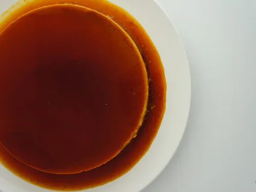 Overhead view of a whole quesillo flan coated in caramel on a white plate