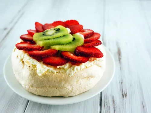An individual pavlova topped with whipped cream, sliced strawberries, and kiwi