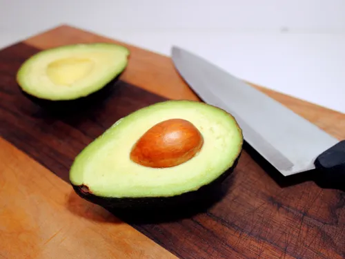 A halved avocado on a wooden cutting board next to a chef's knife
