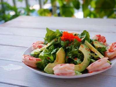A plated salad of romaine lettuce, shrimp, and sliced avocado topped with orange tobiko roe