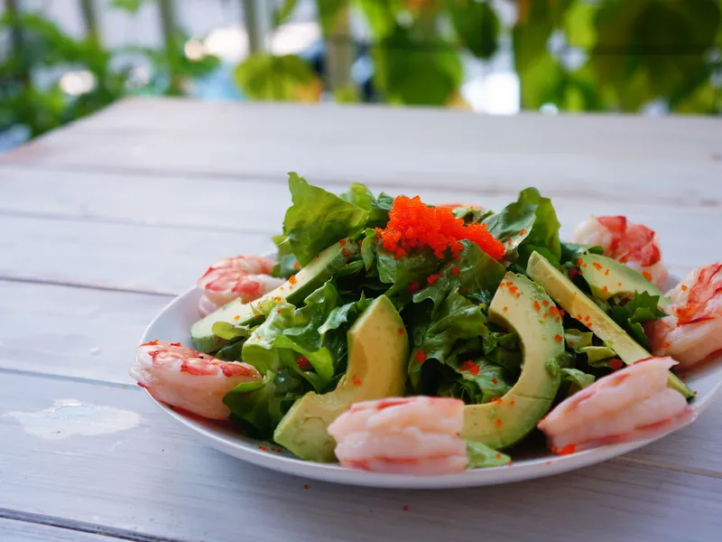 A plated salad of romaine lettuce, shrimp, and sliced avocado topped with orange tobiko roe