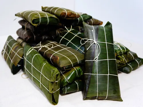 A large pile of hallacas wrapped in plantain leaves and tied with twine, ready to boil