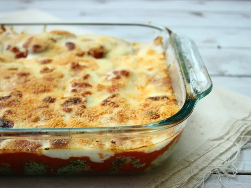 The full pan of baked cannelloni with melted parmesan and tomato sauce visible around the edges